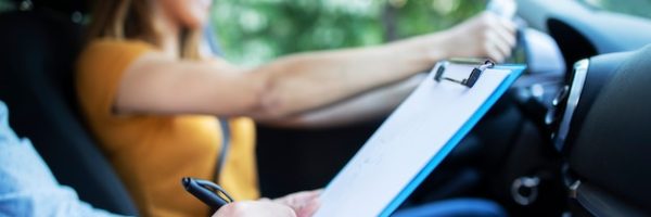 close-up-view-driving-instructor-holding-checklist-while-background-female-student-steering-driving-car_342744-688