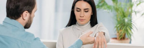 bearded hypnotist holding wrist of young woman with closed eyes during hypnotherapy