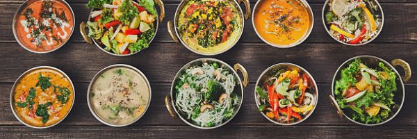 Vegan or vegetarian restaurant dishes top view, hot spicy indian soups, rice and salads in copper bowls. Traditional indian cuisine meal assortment on wood background. Healthy eastern local food