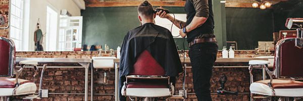 Rear view shot of handsome hairdresser cutting hair of male client. Hairstylist serving client at barber shop.