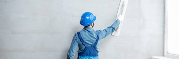 Plasterer in blue working uniform plastering the wall indoors